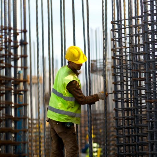 Persona usando implementos de seguridad para construir en acero una estructura de un edificio hecho con barras corrugadas.